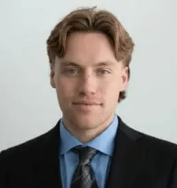 Derek Westwood, REALTOR with SR Group, in a dark suit and light blue shirt against a pale studio backdrop