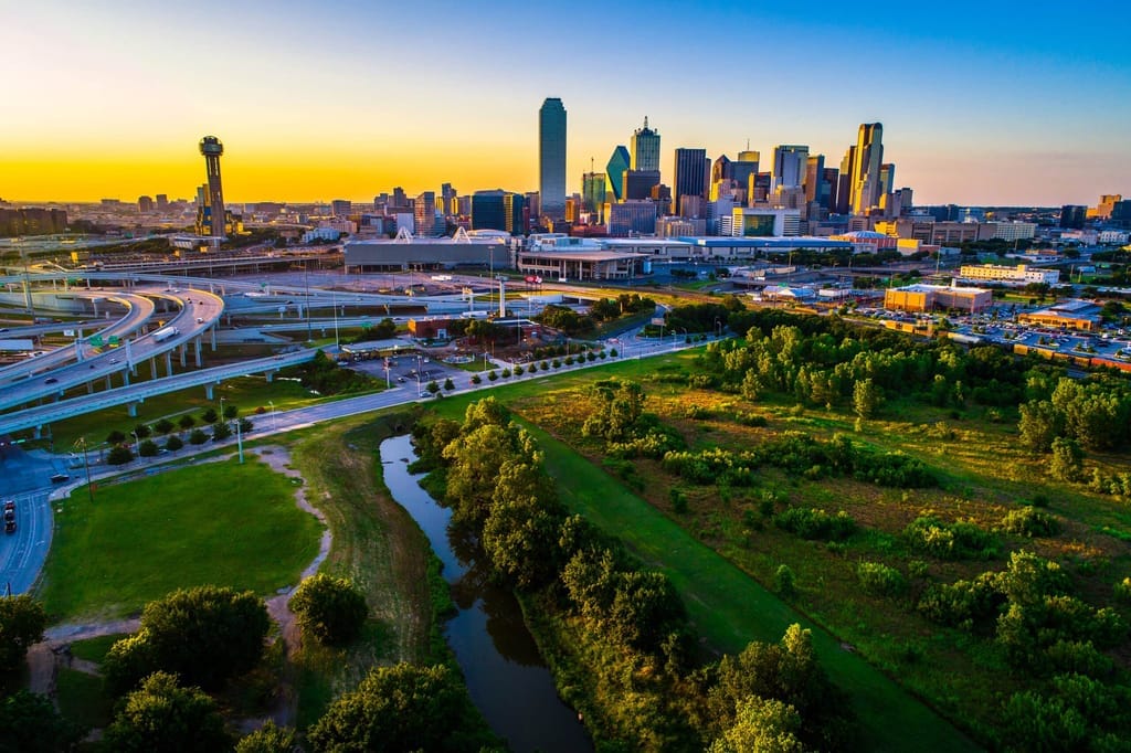 The Dallas skyline at sunrise, Reunion Tower to the left and a green creek corridor below
