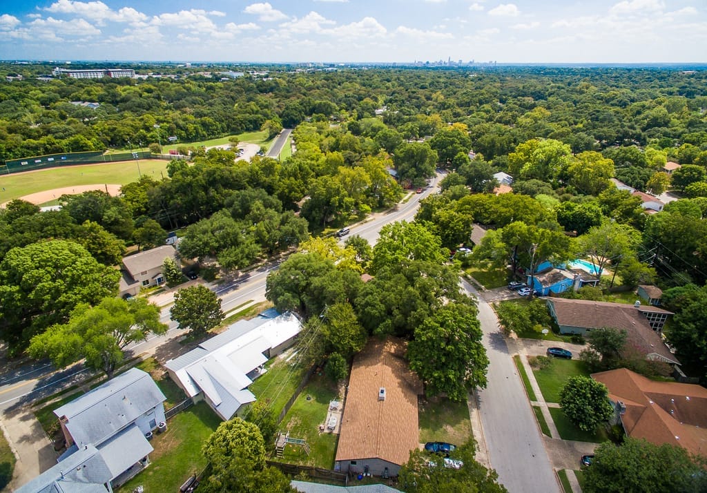 A shaded Allandale street of mid-century ranch houses behind mature live oaks